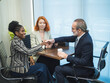 © Singh - professional business set where two individual  woman and man in dark suit, shaking hand across a white table. there tablet and some document. background office environment with minimalistic decor.