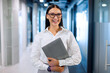 © Home-stock - Portrait of successful businesswoman standing in modern coworking space in hallway and holding laptop, looking and smiling at camera