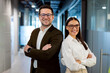 © Home-stock - Positive European business partners posing for portrait at office hallway interior standing back to back with arms crossed, looking at camera and smiling