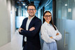 © Home-stock - Positive European business partners posing for portrait at office hallway interior standing back to back with arms crossed, looking at camera and smiling