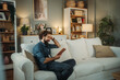 © Dusan - Man laughing reading book on cozy sofa at home