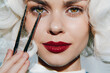 © VICHIZH - Elegant woman with striking makeup holding tweezers, showcasing beauty artistry and vibrant emotions against a minimalist background.