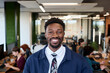 © TrueFrame Collective - Portrait of young adult Black man smiling confidently while standing in modern office workspace, open plan environment with diverse coworkers working at desks in background