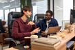 © TrueFrame Collective - Caucasian young adult man explaining project details to Black young adult man while sitting at desk with laptop in modern office, both focused on business discussion