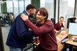© TrueFrame Collective - Caucasian young adult man greeting Black young adult man with handshake and hug in modern office while smiling woman sitting at desk in background laughing and watching interaction