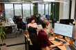 © TrueFrame Collective - Young adult Caucasian women working at desks in modern open plan office, focusing on computer monitors displaying analytics charts, colleagues visible in background