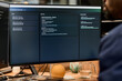 © TrueFrame Collective - Black man sitting at desk working on computer monitor displaying project management dashboard, glass of water and orange on wooden surface, office environment visible in background