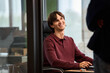 © TrueFrame Collective - Caucasian young adult man sitting at desk smiling and looking up while interacting with standing colleague in modern office environment, using computer keyboard