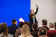 © Anton Gvozdikov - Presenter speaks to large audience on stage with bright blue backdrop. Attentive listeners form rows in conference setting. Energetic mood and clear communication drive the session.