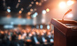 © Shahazadi - A podium with a microphone stands in front of a blurred audience in a large auditorium lit by bright stage lights