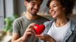 © Laura - Happy young couple celebrating valentine day together faceless, romantic setting, woman and man smiling while holding red heart symbol of love, defocused background, with copy spac