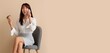 © Pixel-Shot - Asian businesswoman with coffee talking by mobile phone on chair against beige background with space for text