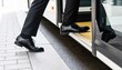 © Netsai - Low-angle shot of a person wearing black dress shoes and suit pants stepping onto the entrance of a bus.
