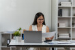 © Kritdanai - Dedicated Professional: An elegant woman, immersed in her work, meticulously examines documents at her workspace, demonstrating her commitment and focus.