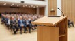 © SOEM - A wooden podium with a microphone in a conference room with a blurred audience in the background.