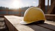 © Thares2020 - A yellow hard hat rests on wooden beams at an outdoor construction site illuminated by warm sunset light with flare