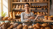 © Unknown OP - Happy female baker standing behind counter full of fresh bread and pastries in bakery shop welcoming customers to buy