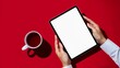 © Raj - Person holding digital tablet with blank white screen on red background near cup of tea, overhead view