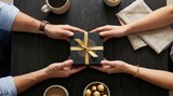 Four hands exchanging a gift box with golden ribbon on a wooden table surrounded by coffee cups and chocolates