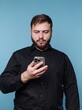 © bodnarphoto - Man in black shirt looking at smartphone against blue background.