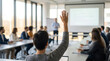© Robert Garcia - Business meeting with a presenter and attendees, one person raising their hand to ask a question. The room has large windows letting in natural light
