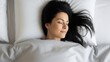 © Eve - Top view of serene brunette woman sleeping deeply in white bed with soft pillows. High angle shot of beautiful female resting peacefully, concept of quality sleep and healthy morning rest.