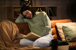 © Pixel-Shot - Beautiful young woman in eyeglasses reading book and sitting on sofa in living room at night
