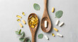 © LORA - Various nutritional supplements and vitamins in capsules on wooden spoons with green leaves on a light background.