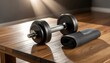 © syaura - A black dumbbell and a rolled mat on a wooden table, ready for a home workout session.