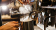© fia - Close-up of a skilled barista frothing milk for coffee, expertly operating a professional espresso machine