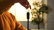 © kinomaster - A person in a yellow sweater is carefully screwing a light bulb into a socket against a warm background.