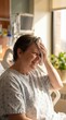 © peacefy - Patient smiles while sitting on a hospital bed, holding a cool compress to her head. Sun light coming in the room. This image captures a moment of peace and optimism during a challenging time.