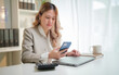 © wattana - Businesswoman checking her smartphone while working at a modern office desk.