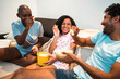 © Nexa - Diverse group of young friends laughing and eating popcorn during a movie night at home, sitting on a couch in casual wear.