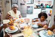 © Nexa - Happy African American family having breakfast together at home. Grandmother and granddaughter eating morning meal in the kitchen.