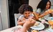 © Nexa - Happy little African American girl smiling while having breakfast with her family at home.