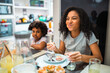 © Nexa - Happy African American sisters enjoying a meal together at home, with the older girl making a funny face while eating.