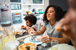 © Nexa - Happy African American sisters enjoying a healthy breakfast together in a modern kitchen, laughing and talking while eating.