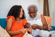 © Nexa - Happy African American grandmother and granddaughter crocheting together on a sofa at home, sharing a joyful moment and learning a traditional craft.