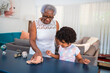 © Nexa - Senior African American grandmother teaching her young granddaughter how to clean a table in a modern living room, fostering bonding and responsibility through household chores.