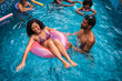 © Nexa - Happy young multiethnic couple and friends having fun in a swimming pool with inflatable rings during a summer vacation.