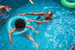 © Nexa - Happy African American mother teaching her daughter to swim in a pool with an inflatable ring during summer vacation.