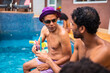 © Nexa - Diverse group of friends enjoying cocktails and conversation by a swimming pool on a sunny summer day.