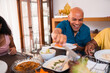 © Nexa - Cheerful mature African American man laughing while enjoying a healthy meal with family at home.