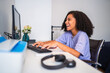 © Nexa - Cheerful young woman with curly hair laughing while working on a computer at her home office desk.