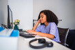 © Nexa - Young African American woman working from home at her desk with a computer and headphones.