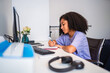 © Nexa - Young Black woman with curly hair writing in a notebook while studying at her desk in a home office.
