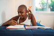 © Nexa - Young Black woman with a shaved head lying on her bed and studying, writing in a notebook at home.