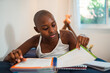 © Nexa - Focused young Black woman with a shaved head lying on her bed and studying from a notebook at home.