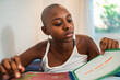 © Nexa - Focused young African American woman with a shaved head reviewing educational materials in a notebook at home.